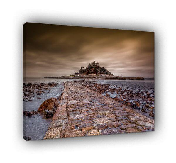 St Michael’s Mount: The Ancient Crossing The Scene Captured from a dramatic low-angle perspective, this photograph emphasizes the incredible texture of the historic granite causeway. As the tide begins to turn, the wet cobblestones glisten, creating a rugged path that leads the viewer’s eye directly toward the silhouette of the medieval castle. This perspective makes the viewer feel as though they are standing at the very edge of a journey between the mainland and the mythic island. The Atmosphere Utilizing a long-exposure technique, the sky is transformed into a sweeping canopy of motion. The blurred clouds create a sense of time passing, as if capturing centuries of Cornish history in a single frame. The mood is intentionally 