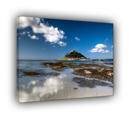 St Michael’s Mount: Sapphire Reflections The Scene This vibrant landscape captures St Michael’s Mount in all its coastal glory during a bright, clear day. Taken at low tide from the Marazion shoreline, the image highlights the breathtaking clarity of the Cornish waters. In the foreground, shallow pools of crystalline water rest upon the pale sands, creating a natural mirror that reflects the passing white clouds and the deep blue of the sky. The Atmosphere While our 